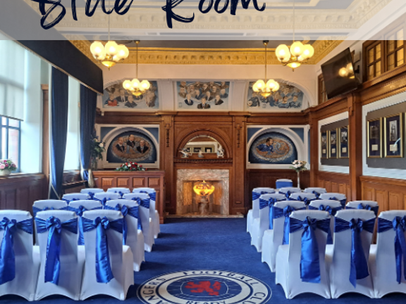 Wood panelled room with blue carpet and white chairs with blue ribbons set our theatre style with an isle running down the middle. Text reads Blue Room.