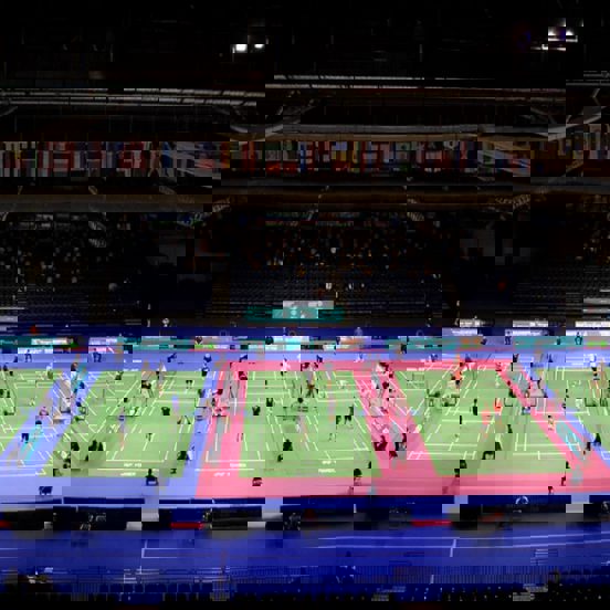A view of five badminton courts, national flags hang from the ceiling.