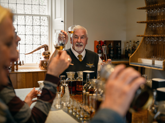 Man wears a jumper with Glengoyne logo on it and is take people through a tasting of whisky. 