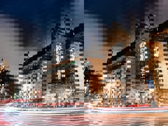 Grey stone building with turrets on either side of the wooden and glass door. Above teh door is an imposing stone balcony and large stained glass window. 