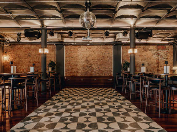 Large room with checkerboard style flooring with table and chairs along each side. Glitterball hangs from the ceiling.