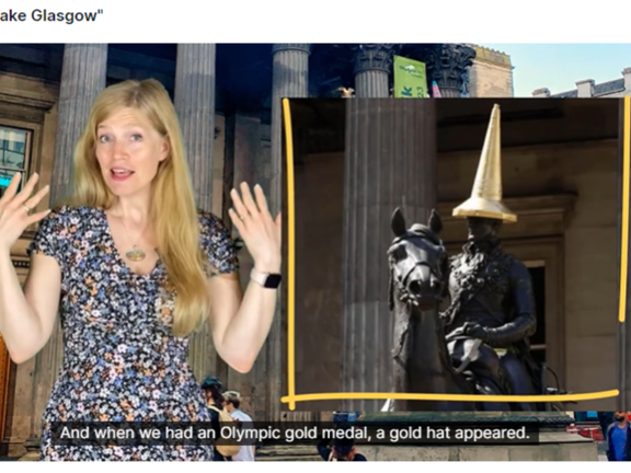 Screenshot of a virtual tour of Glasgow. Presenter stands in front of a building known as the Gallery of Modern Art. To the right is an inset image of a well known statue of a man on a horse. The man is wearing a golden traffic cone on top of his head like a hat. Along the bottom of the screen captions read: and when we had an Olympic gold medal, a gold 'hat' appeared. The title reads: People Make Glasgow