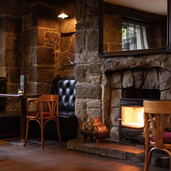 Cosy pub interior with leather seating, exposed stone wall and a small log burning stove