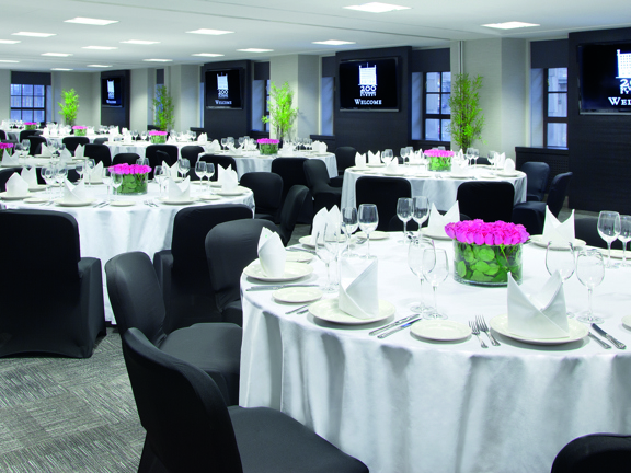 The St Andrews Suite laid out in banquet style seating. A large room full of multiple round tables are covered in white table cloths. There are vases of cut flowers, wine glasses and napkins visible on the tables.