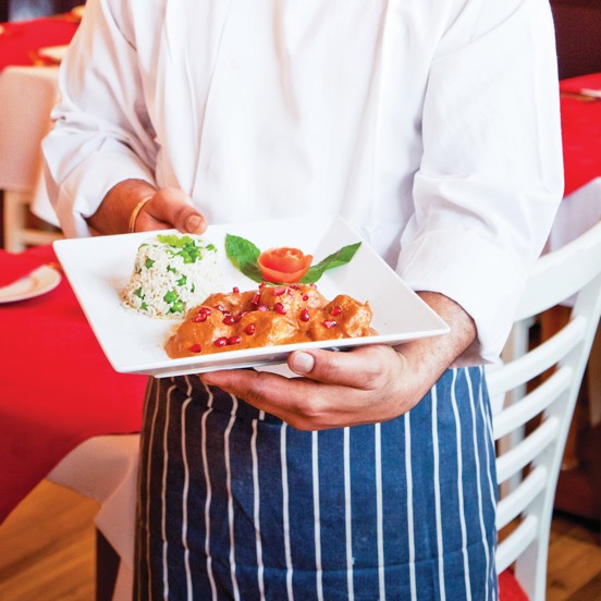 Person holding a white plate with artfully arranged rice and curry