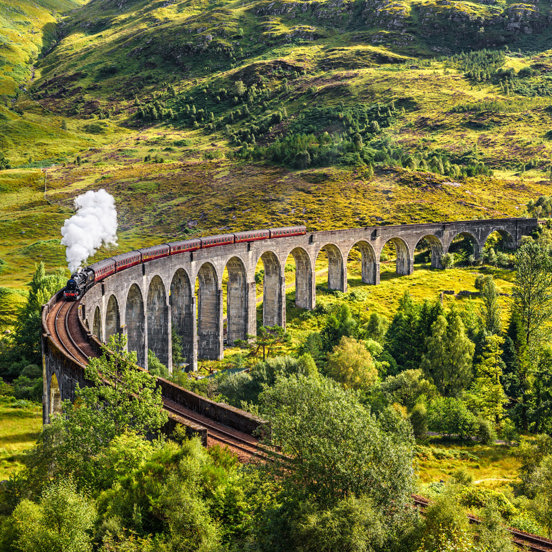 Jacobite steam train crossing the Glenfinnan viaduct, surrounded by greenery