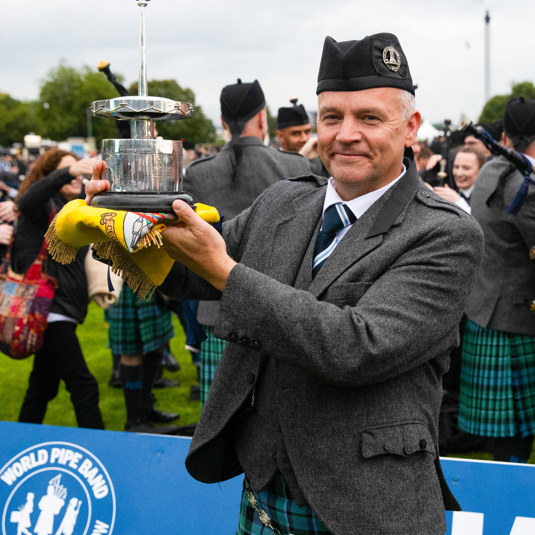 Member of the pipe band showing the winning trophy