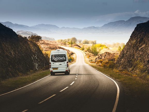 Mini coach driving away with Rabbie's written across back windows and hills ahead