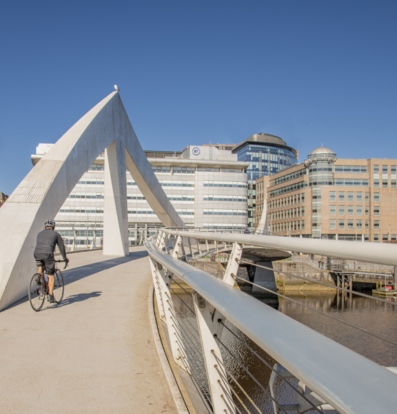 cyclist crossing the Tradeston Bridge in the sunshine, with office building in the background