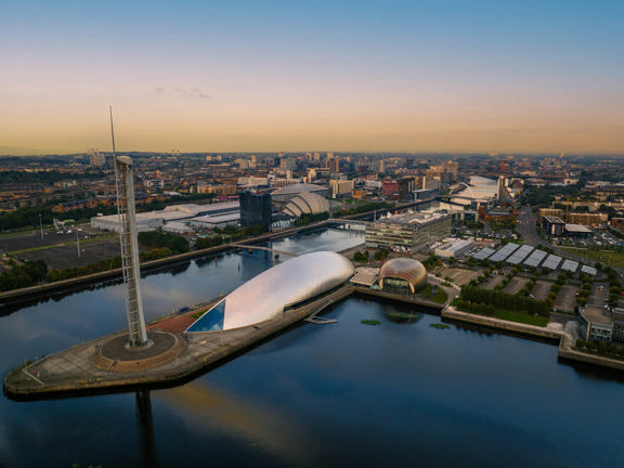 Cityscape with the River Clyde, the tall metal spire of the Glasgow Tower, of the crescent-shaped metal structure of the Glasgow Science Centre and of the round glass fronted IMAX theatre, and the modern structures of the SEC Campus