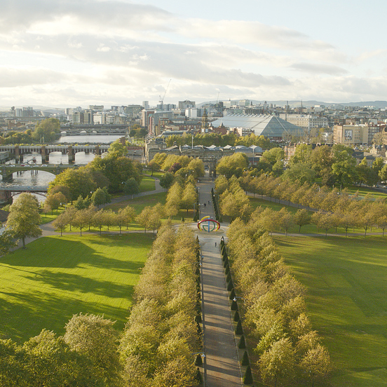 Sunny view of the tree-lined paths of Glasgow Green, on the bank of the River Clyde with 4 bridges and Glasgow city centre in the background