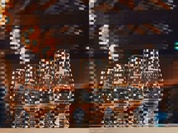 Four whisky tasting glasses are lined up on a bar each with a nip of whisky. 