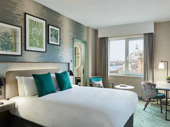 Hotel bedroom with large double bed accents of green in the soft furnishings. 