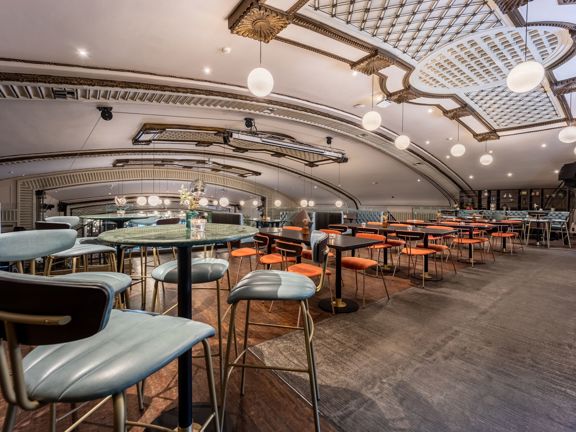 Large room with square and circular tables with orange and grey seats. 