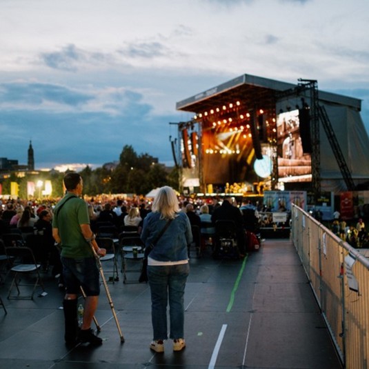 An attendee using crutches watches the TRNSMT main stage from the accessible area with a woman
