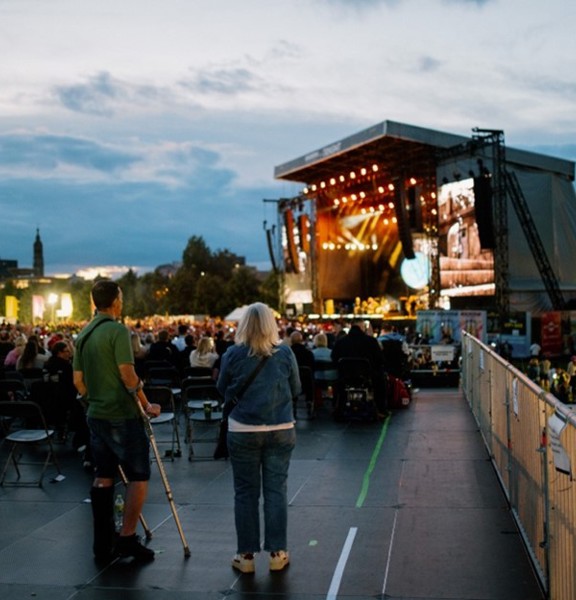 An attendee using crutches watches the TRNSMT main stage from the accessible area with a woman