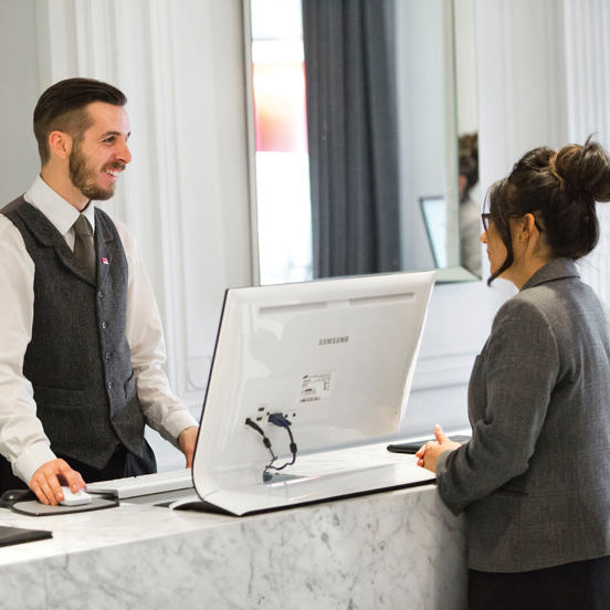A man smiling at a woman across a reception counter, with a computer monitor between them