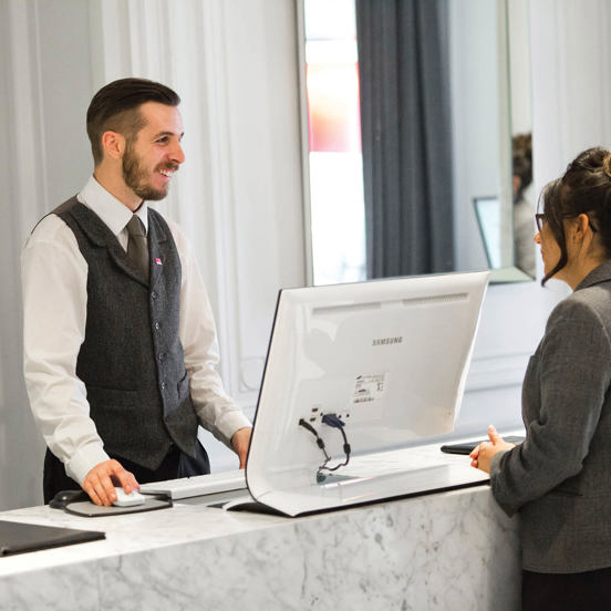 A man smiling at a woman across a reception counter, with a computer monitor between them