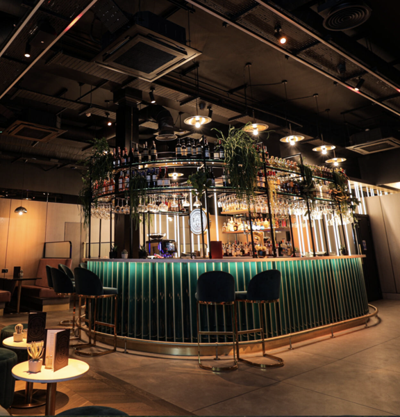 Room with a green titled bar at the centre, various tables and chairs laid out across the room. 