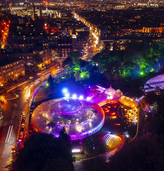 An aerial view of the botanic gardens in the west end lit up at night time blue, purple, orange and green for GlasgGlow 