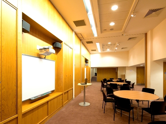 Room with large white screen, round tables and chairs.