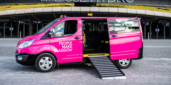 pink taxi with People Make Glasgow branding in front of a modern concert arena, with the ramp down