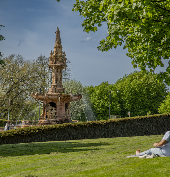 A couple lazing in the sunshine near the large terracotta, five-tier, French Renaissance-style Doulton Fountain in Glasgow Green