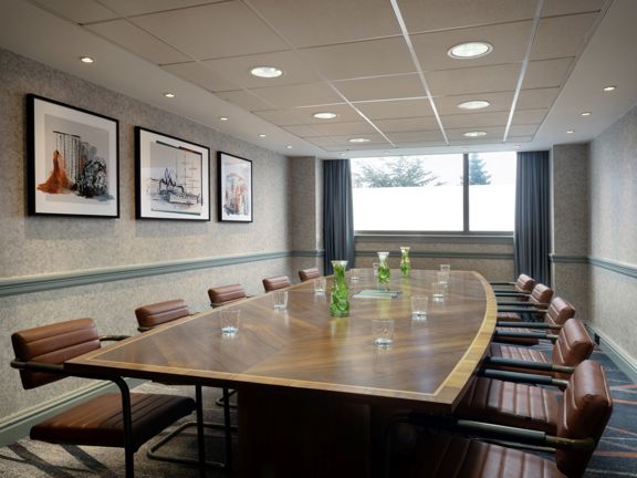 Modern boardroom with large wooden table surrounded by ten brown leather chairs.