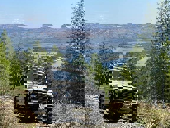 Land Rover driving up a steep hill, Loch Lomond and hill sin the background. 