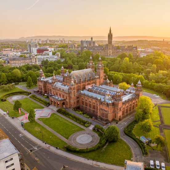 Aerial view of Kelvingrove Art Gallery and Museum in Glasgow at sunset, surrounded by Kelvingrove Park with the University of Glasgow and city skyline in the distance.