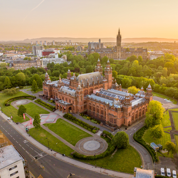 Aerial view of Kelvingrove Art Gallery and Museum in Glasgow at sunset, surrounded by Kelvingrove Park with the University of Glasgow and city skyline in the distance.