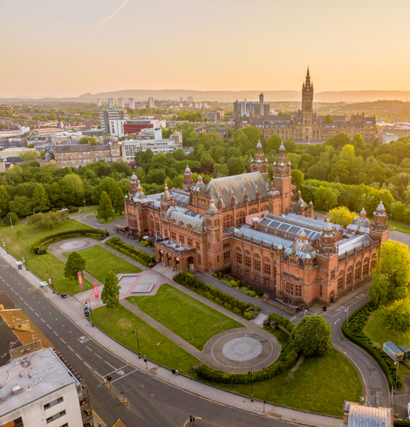 Aerial view of Kelvingrove Art Gallery and Museum in Glasgow at sunset, surrounded by Kelvingrove Park with the University of Glasgow and city skyline in the distance.