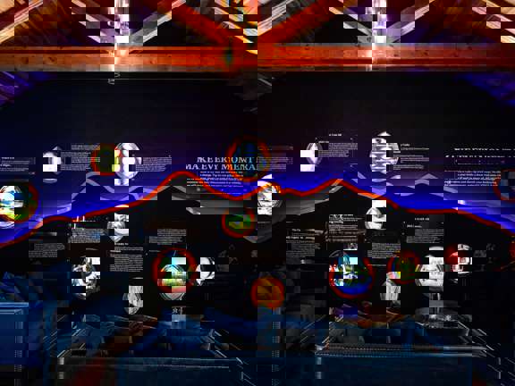 A dark and moody room with dark blue walls and dark blue velvet sofas. Circular pictures are back lit along the wall at varying heights. A sign reads Make Every Moment Raer. 