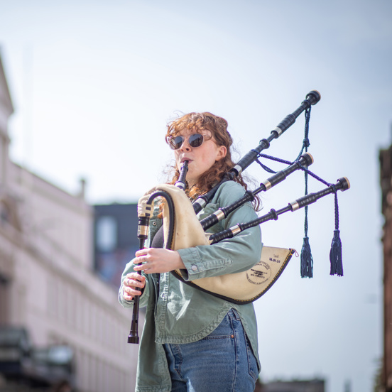A bagpiper wearing sunglasses performs on a city centre street in Glasgow.