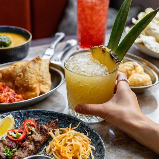 Various Indian food dishes on a table with exotic juice drinks.  