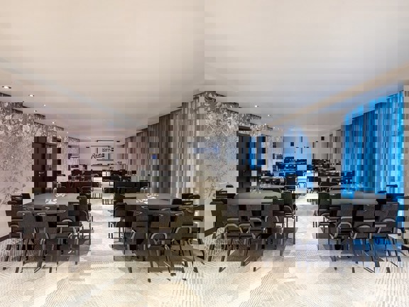 Bright and light hotel meeting room at Radisson Blu with dark grey banquet chairs set up cabaret style and floor to ceiling windows.