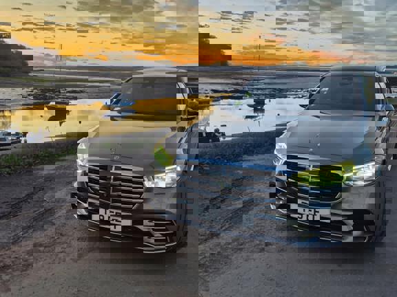 Silver Mercedes car on a pier with a backdrop of sunset, water and sailing boats