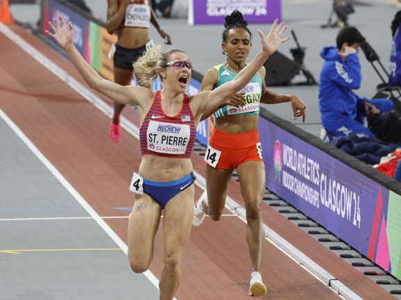 Athlete crosses finish line cheering with both arms raised in the air.