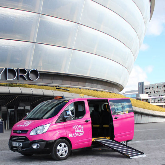 pink taxi with People Make Glasgow branding in front of a modern concert arena, with the ramp down