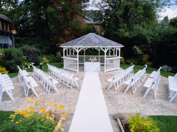 Gazebo, white chairs set up in rows facing the gazebo and a white carpet runner runs along the middle of the chairs into the gazebo.