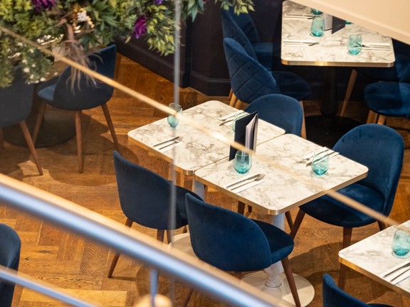 View of restaurant from internal balcony overlooking marble tables, velvet chairs and bouquets of flowers.