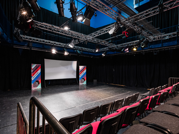 Theatre space with raked seating and big screen with roller banners on either side. 