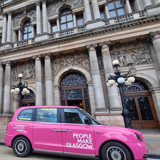 An image of 3 pink People Make Glasgow taxis in various sizes parked outside Glasgow's City Chambers.