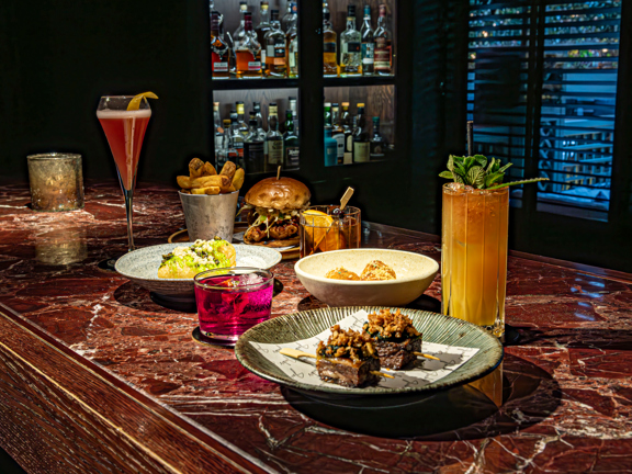 Red marble bar top laid with sumptuous plates of food and cocktails. 