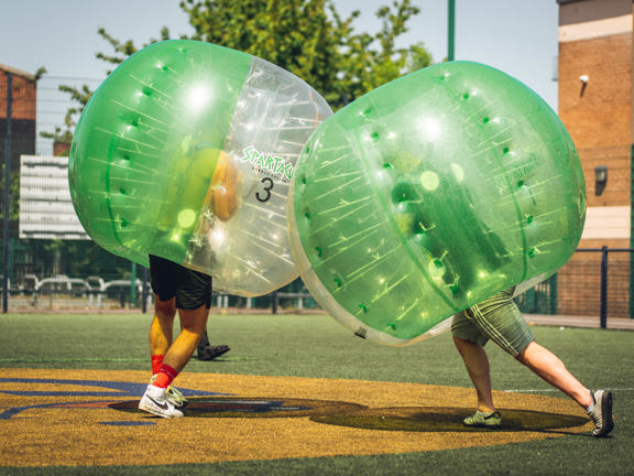 Two people inside giant inflatable footballs. 