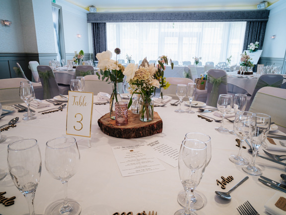 Beautiful table arrangements of natural flowers in various containers, wooden place names and silver cutlery and glassware. 