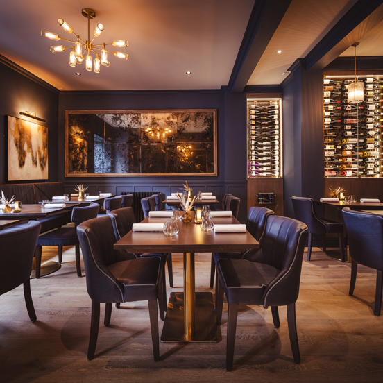 Navy blue interior of a restaurant with gold accents, leather chairs and dark wooden tables. 