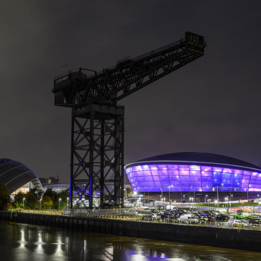 A nightscape scene of the OVO Hydro lit up and the Finneston Crane