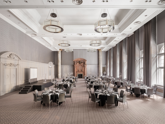Interior of Grand Ballroom in hotel - large windows flood the space with daylight. Tables and chairs are set up for a dinner, stage and screen to the left hand side and a large ornate fireplace at the far end of the room.  