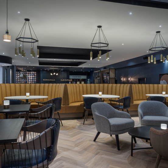 Hotel bar with dark wooden tables, mustard banquette seating and mixed seating. 